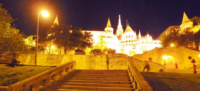 Illuminated Fisherman's Bastion at night with stone staircase in foreground, warm yellow lighting on white towers and spires against dark sky, Budapest, Hungary