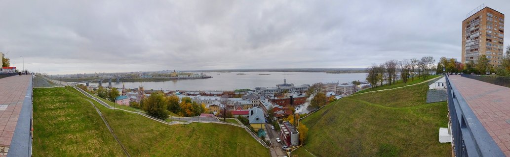 Wide panoramic view of Nizhny Novgorod showing green hills, Volga River, city buildings, and cloudy sky from elevated viewpoint