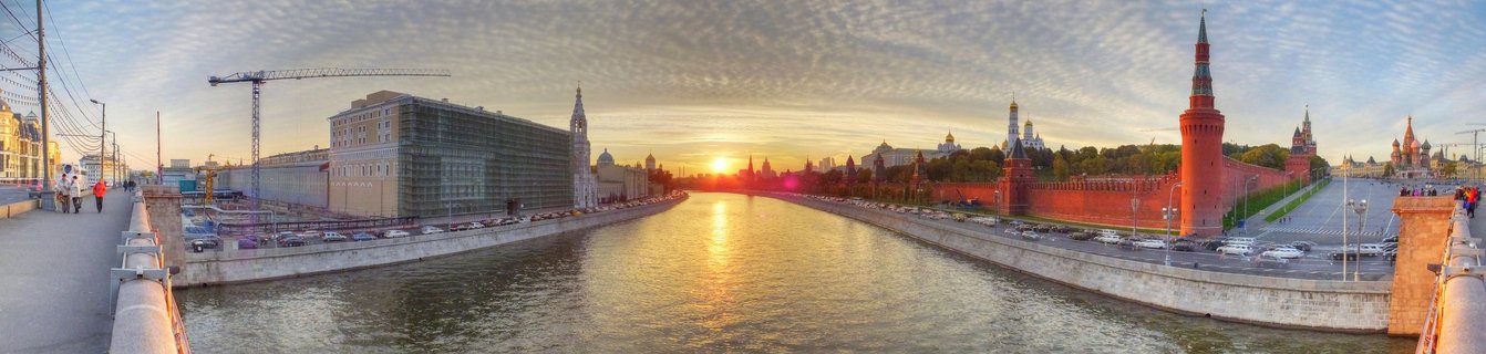 Panoramic view of Moscow Kremlin red walls and towers along the Moskva River at sunset with golden sky and clouds