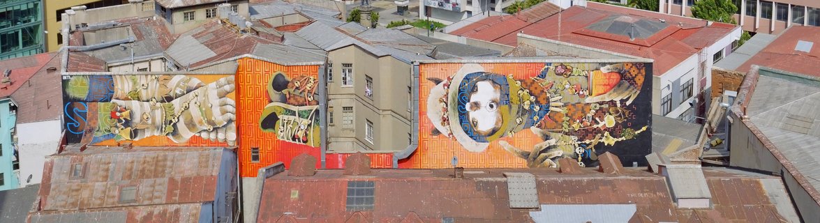 Aerial photograph showing two large colorful murals painted on building walls in Santiago, Chile, surrounded by red rooftops and urban architecture