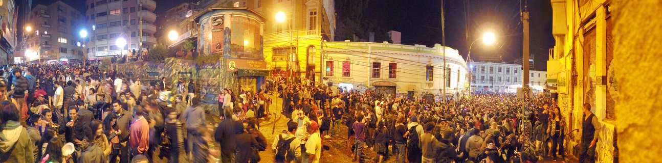 Large crowd of people gathered on a city street at night in Santiago de Chile, with illuminated buildings and streetlights visible