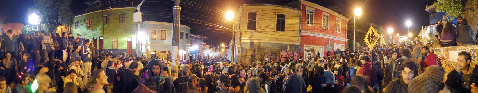Large crowd of people gathered on a street at night during a celebration, with colorful painted buildings and street lamps in the background