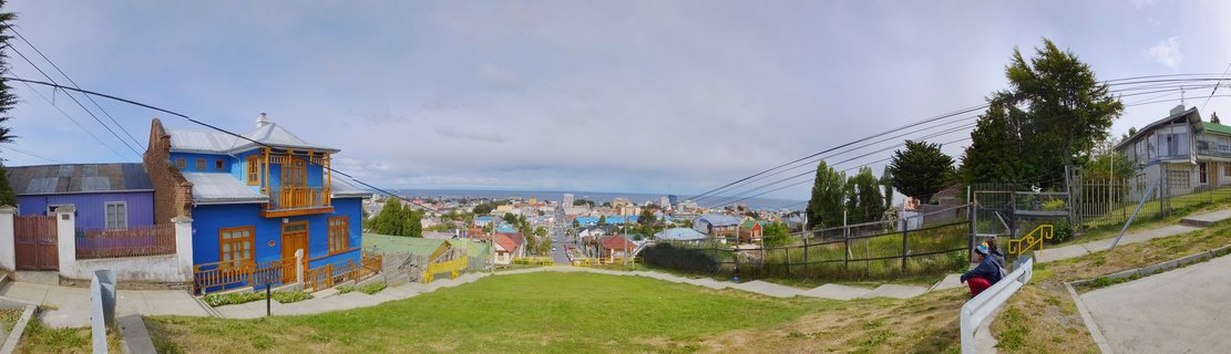 Wide view of colorful houses on a hillside in Puerto Natales Chile with a bright blue wooden house in foreground overlooking the city and water beyond under cloudy sky