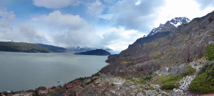 Wide landscape view of a glacial lake with icebergs, surrounded by mountains with snow-capped peaks under a cloudy sky in Torres del Paine National Park, Chile