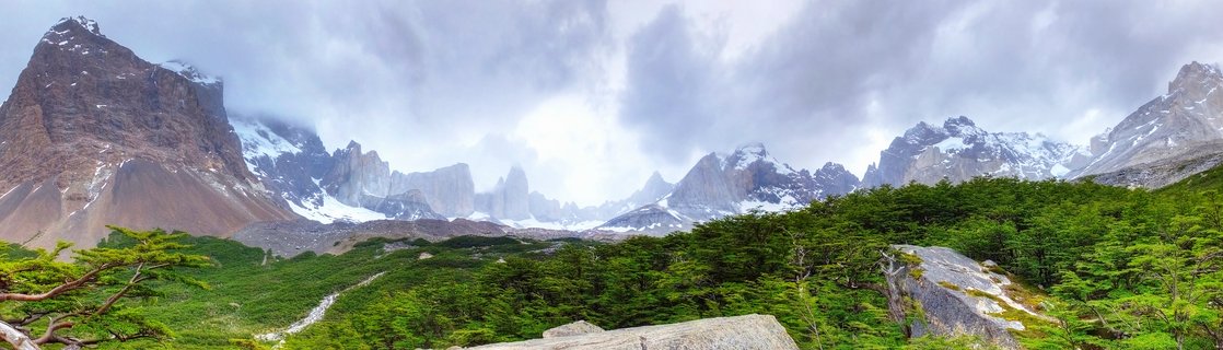Mountain landscape showing granite towers and snow-capped peaks rising above green forest in Torres del Paine National Park, Chile