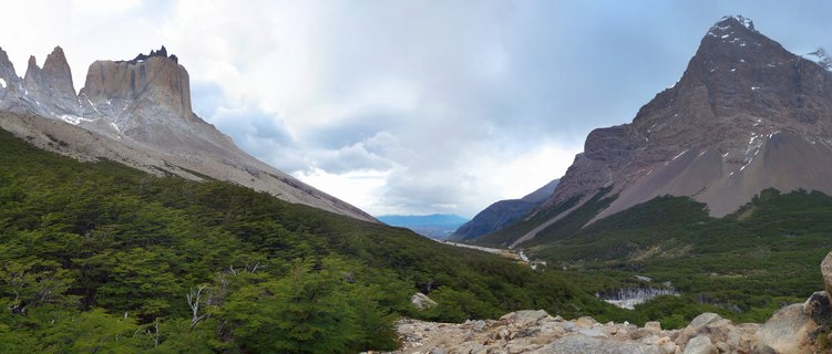 Granite mountain towers of Torres del Paine rising above green forest valley in Chilean Patagonia under cloudy sky