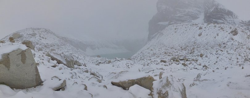 Snow-covered rocky landscape with granite mountain peaks and a glacial lake visible through fog in Torres del Paine National Park, Chile