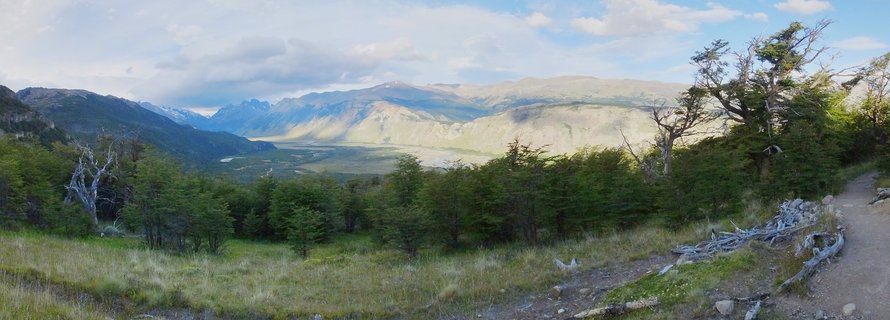Mountain landscape showing forested hills, a wide valley, and distant peaks under cloudy skies in Patagonia, Argentina