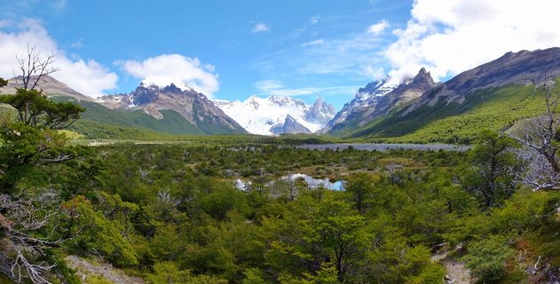 Snow-capped mountain peaks of Fitz Roy massif rising above green forest valley with small pond in Patagonia, Argentina