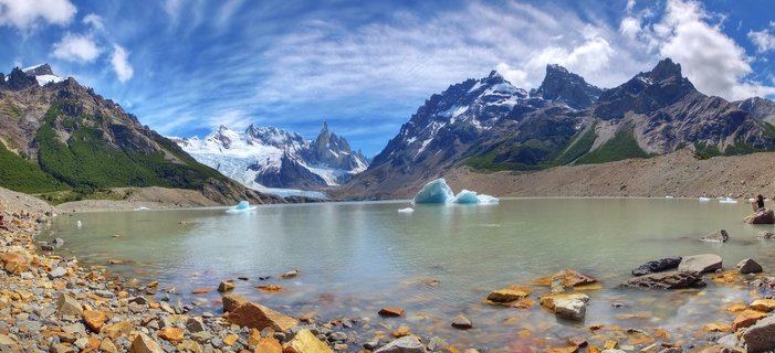Panoramic view of Mount Fitz Roy and jagged mountain peaks rising above a turquoise glacial lake with floating icebergs and rocky shoreline in Patagonia, Argentina