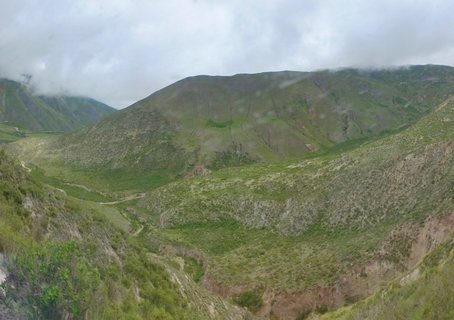 Green mountain valley with winding dirt road through rugged hillsides under cloudy sky in Salta, Argentina