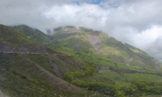 Green mountain landscape with a winding road, cloudy sky, and exposed earth formations in Salta, Argentina