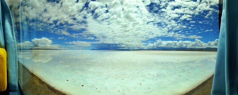Panoramic view of white salt flat extending to distant mountains under blue sky with white clouds in Atacama Desert
