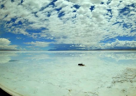 Vast salt flat with shallow water reflecting dramatic white clouds and blue sky, distant mountains on horizon, San Pedro de Atacama, Chile