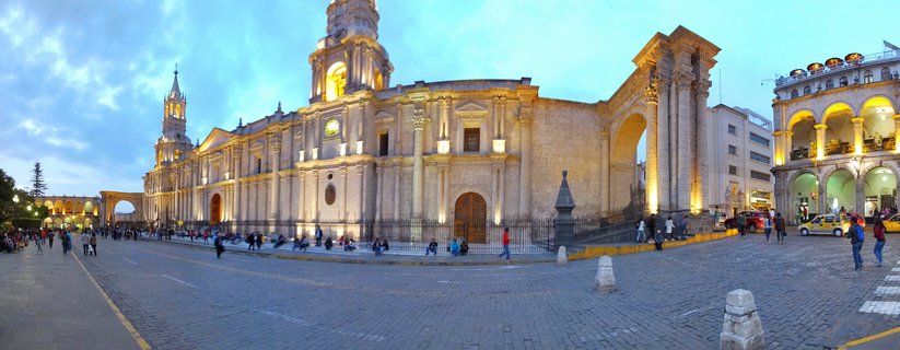 Illuminated colonial cathedral with twin bell towers at twilight in a cobblestone plaza with pedestrians in Arequipa, Peru