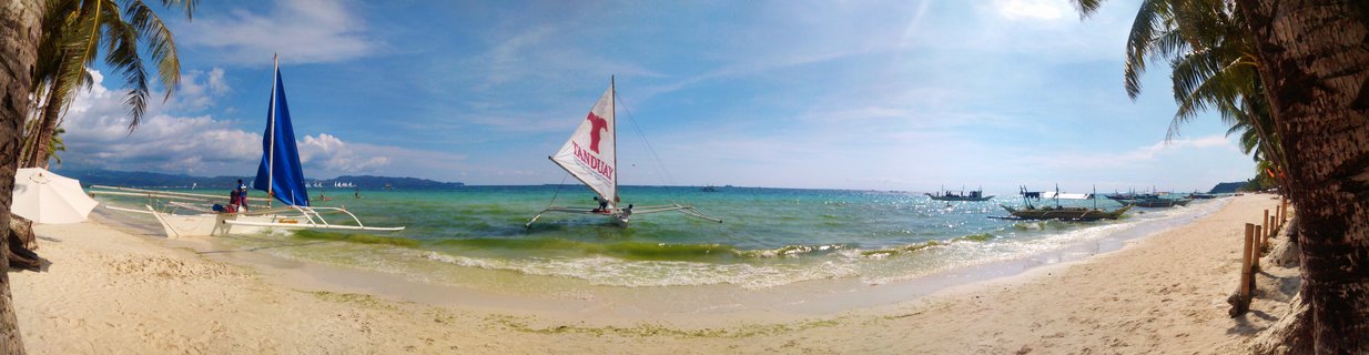 White sand beach with palm trees, traditional Filipino outrigger sailboats with blue and white sails in turquoise ocean water, blue sky with clouds, Boracay Philippines
