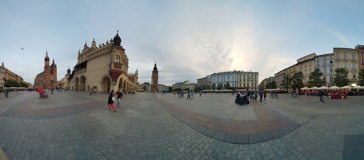 Panoramic view of Krakow's Main Market Square showing the Cloth Hall building, St. Mary's Basilica towers, cobblestone pavement, and pedestrians walking across the historic plaza