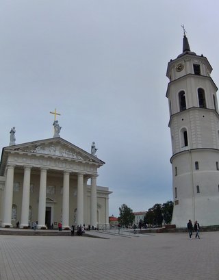 White neoclassical cathedral with six columns and golden cross alongside tall white bell tower with clock at Cathedral Square in Vilnius, Lithuania under overcast sky