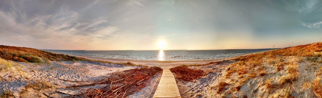 A wooden boardwalk path through sand dunes with beach grass leading to the Baltic Sea at sunset