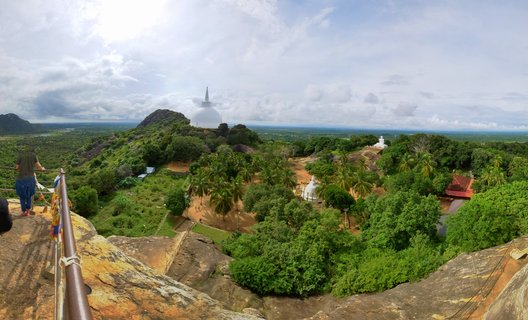 Elevated panoramic view of white Buddhist stupas in Polonnaruwa, Sri Lanka, with tropical trees, rocky foreground, and cloudy sky
