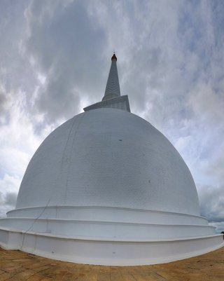 Large white Buddhist stupa with dome-shaped structure and tall pointed spire with golden tip against cloudy gray sky