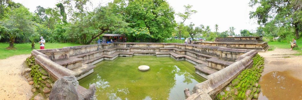 Ancient rectangular stone bathing pool with green water, stone steps, tropical trees, and visitors at Polonnaruwa archaeological site in Sri Lanka