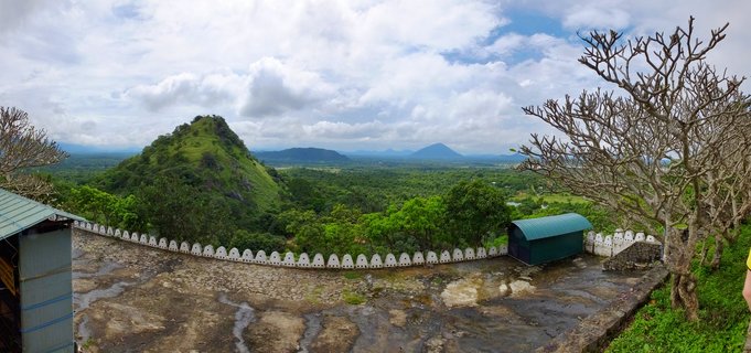 Stone terrace with white decorative wall overlooking green tropical landscape with hills and mountains under cloudy sky at Dambulla, Sri Lanka