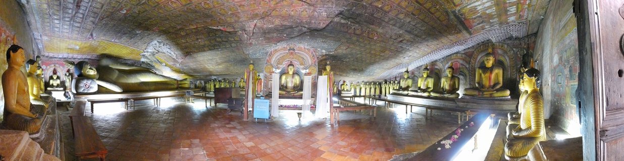 Interior of cave temple with multiple golden Buddha statues in seated and reclining positions, painted ceiling with traditional Buddhist murals, terracotta tile floor
