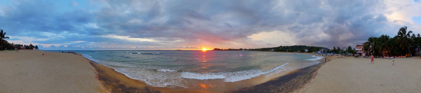Panoramic beach sunset at Hikkaduwa, Sri Lanka showing ocean waves, sandy shore, palm trees, dramatic cloudy sky with golden sun on horizon, and people walking on beach