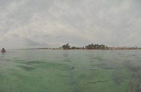 Ocean water view looking toward a tropical beach coastline with palm trees, buildings, and cloudy sky in Hikkaduwa, Sri Lanka