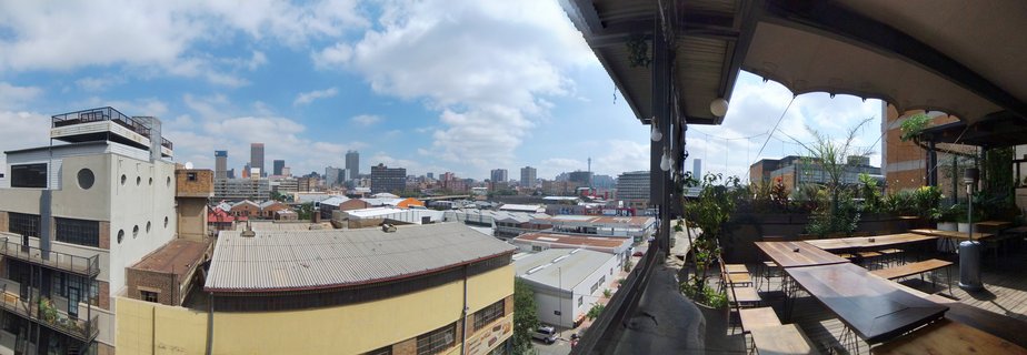Rooftop terrace with wooden tables overlooking Johannesburg city skyline with buildings and blue sky with clouds