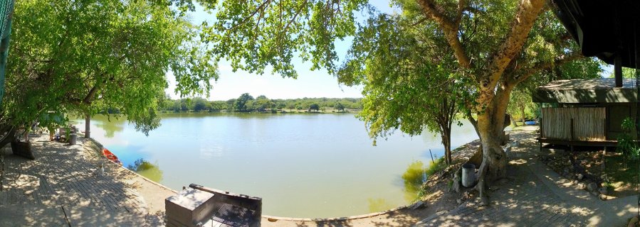 Safari lodge patio with braai grill overlooking a calm waterhole surrounded by trees at Kruger National Park