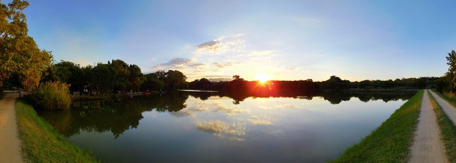 Sunset over a calm dam with tree-lined horizon and dirt roads on both sides, Kruger National Park