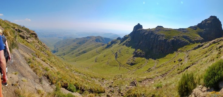 Mountain landscape showing a hiker on a rocky trail with green valleys and steep cliffs in the Northern Drakensberg, South Africa