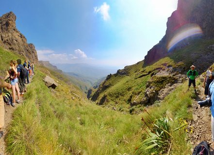 Group of hikers walking on a mountain trail between rocky cliffs in the Drakensberg mountains with green grassy slopes and valley views