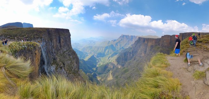 Hikers stand at the cliff edge overlooking the dramatic Amphitheatre rock formation and Tugela Falls in Northern Drakensberg's Royal Natal National Park, South Africa.
