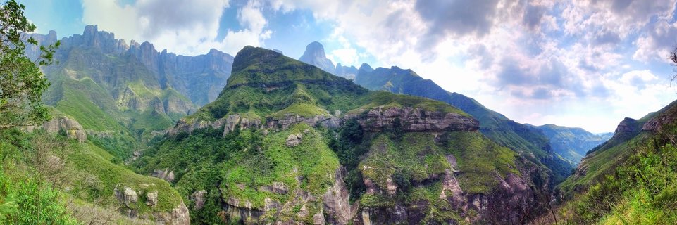 Clear mountain stream flowing around large smooth boulders with a small waterfall and mountain cliffs in the background