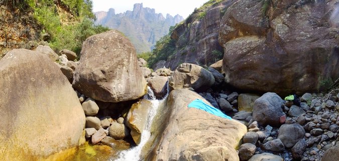 Small waterfall flowing over large boulders in a rocky mountain stream with Drakensberg peaks visible in the background