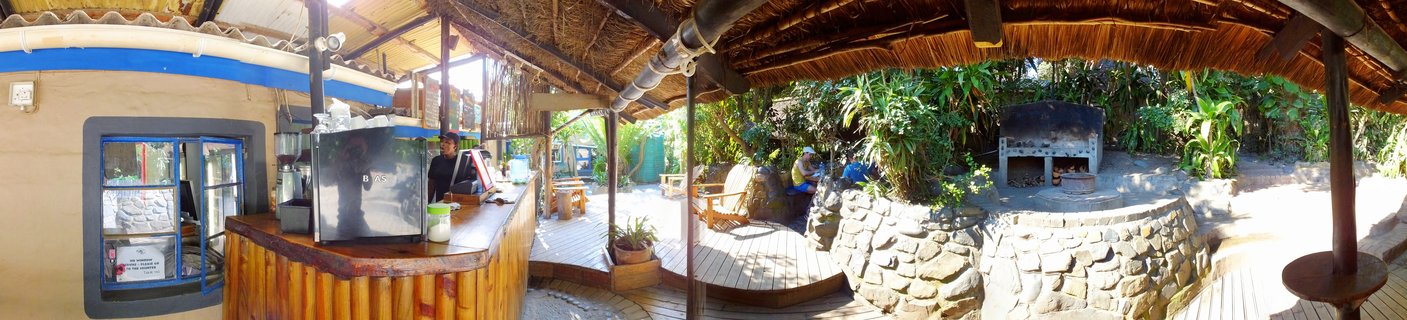 Outdoor bar area with thatched roof, wooden deck, stone walls, and tropical plants at a lodge in Coffee Bay, South Africa