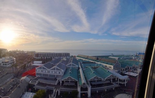 Elevated panoramic view of Victoria & Alfred Waterfront in Cape Town showing green-roofed buildings, harbor, ocean horizon, and Table Mountain in the distance during golden hour sunset