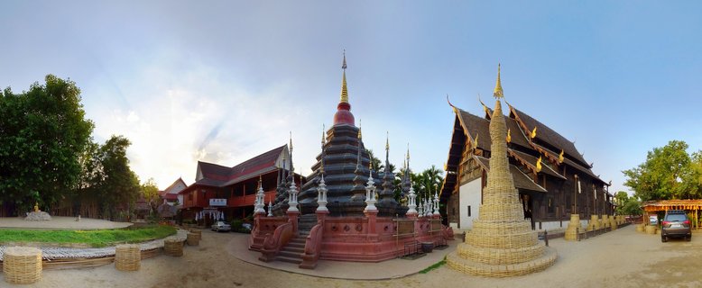 Buddhist temple complex in Chiang Mai featuring multiple ornate stupas with golden spires, traditional wooden temple buildings with tiered roofs, and temple grounds under a clear blue sky
