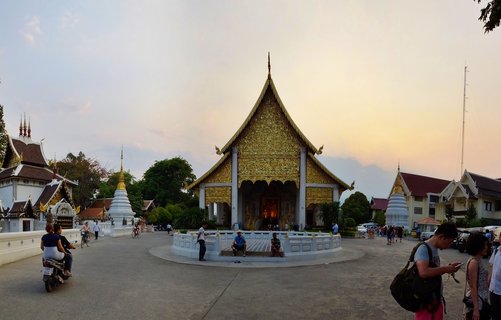 Buddhist temple with golden ornate gable and white stupas surrounded by visitors at sunset in Chiang Mai Thailand