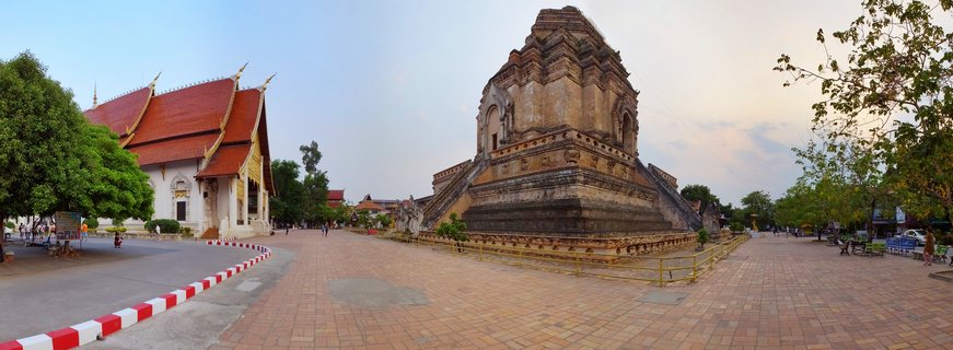 Wide view of Wat Chedi Luang Buddhist temple showing large brick chedi stupa and red-roofed prayer hall with visitors walking on brick courtyard in Chiang Mai Thailand