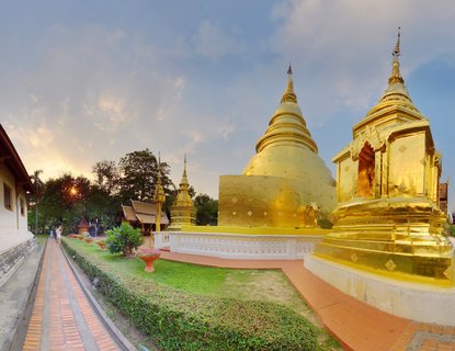 Golden Buddhist temple stupas with manicured gardens, brick pathways, and traditional Thai architecture during sunset