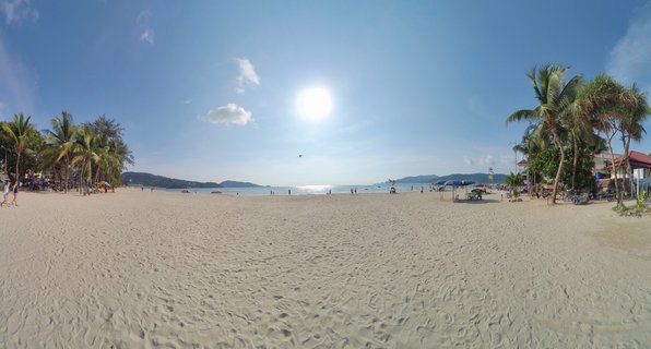 Panoramic beach scene showing wide expanse of white sand with palm trees on both sides, ocean in the distance, people walking on beach, blue sky with bright sun overhead, Phuket Thailand