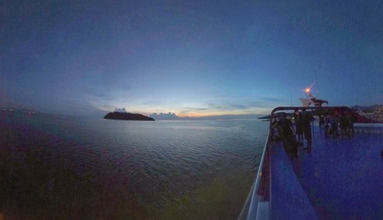 Ferry boat deck with passengers at dusk, ocean view with distant island silhouette and twilight sky over Gulf of Thailand