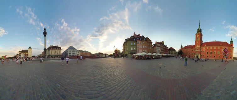Wide panoramic view of Castle Square in Warsaw showing Sigismund's Column on the left, the red Royal Castle with clock tower on the right, cobblestone pavement, and visitors walking across the plaza under a blue sky with scattered clouds