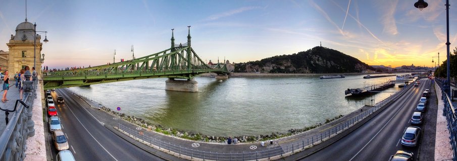 Panoramic view of the green Liberty Bridge crossing the Danube River in Budapest at sunset, with Gellért Hill and city skyline in the background
