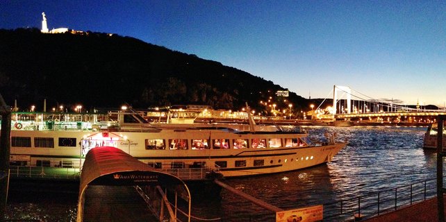 River cruise ships on the Danube River at dusk in Budapest with illuminated Elisabeth Bridge and Liberty Statue on Gellért Hill in the background
