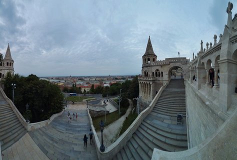 White stone staircases and conical turrets of Fisherman's Bastion in Budapest with tourists walking and city view in background under overcast sky